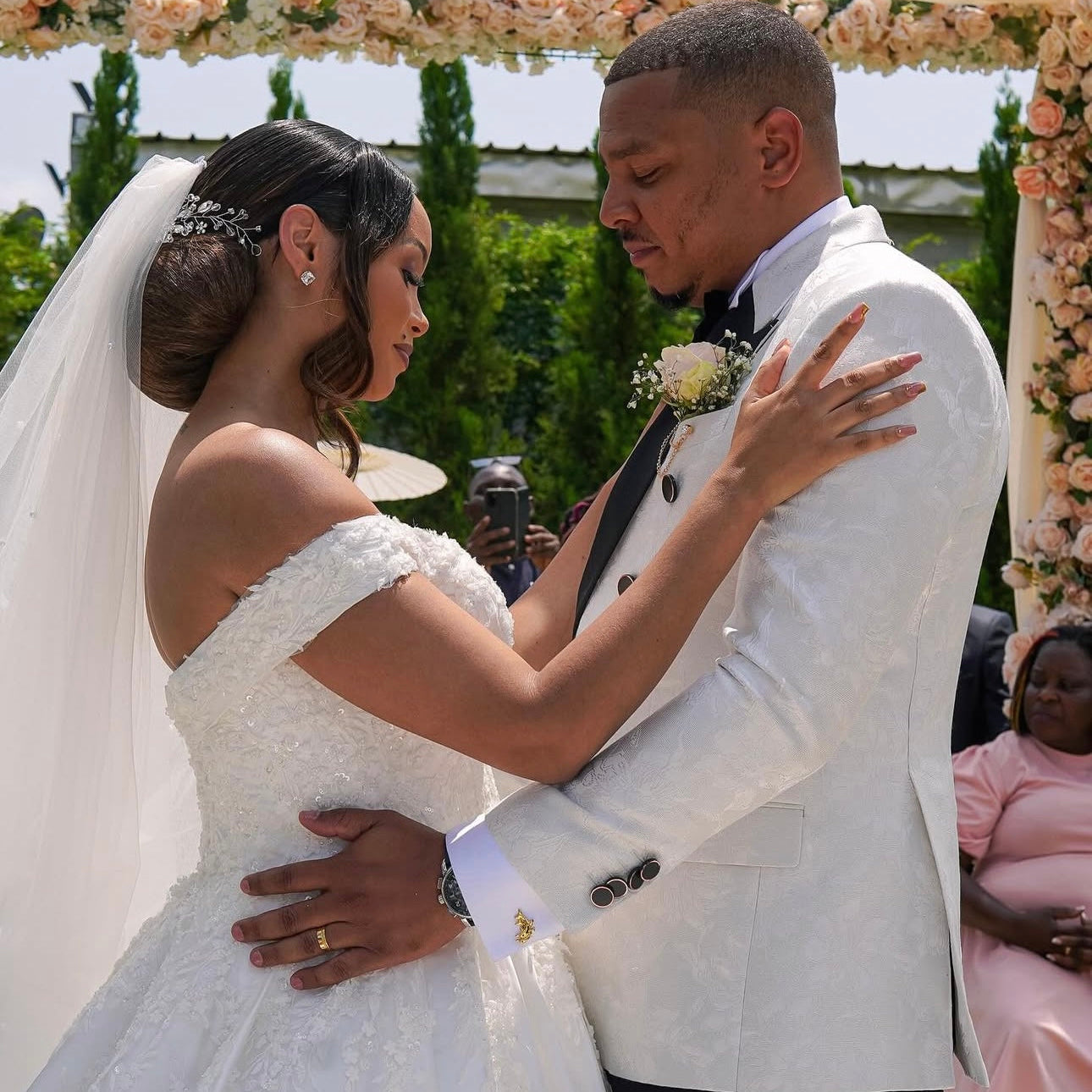 Couple in wedding attire standing under a floral archway